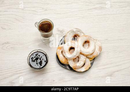 Ciambelle cosparse di zucchero in polvere, caffè fresco e marmellata su un piano di legno chiaro fone.Vid Foto Stock