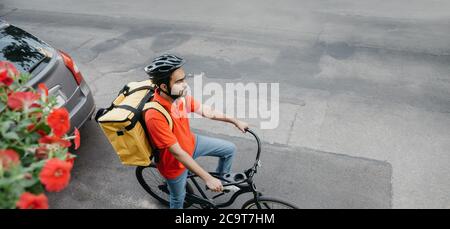 Servizio di consegna online. Corriere in casco con grande zaino giallo in bicicletta Foto Stock