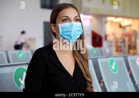 Primo piano giovane donna in attesa del suo volo seduto in aeroporto lounge indossare maschera chirurgica. Ragazza viaggiatore con maschera protettiva sul viso all'aeroporto. Foto Stock