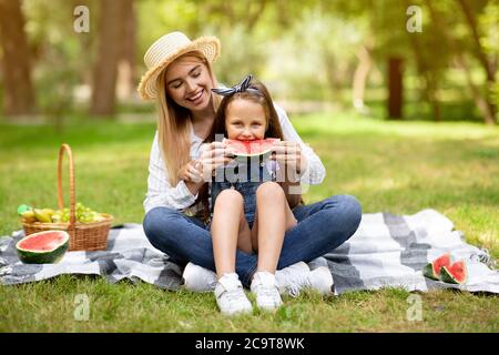 Gioiosa Madre che nuote la figlia che mangia il cocomero al picnic all'aperto Foto Stock