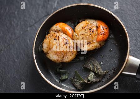 Due capesante di re, Pectens maximus, con le loro arance, che sono state fritte in una piccola padella antiaderente con burro e foglie di salvia. Dorset it Foto Stock