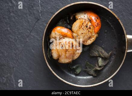 Due capesante di re, Pectens maximus, con le loro arance, che sono state fritte in una piccola padella antiaderente con burro e foglie di salvia. Dorset it Foto Stock
