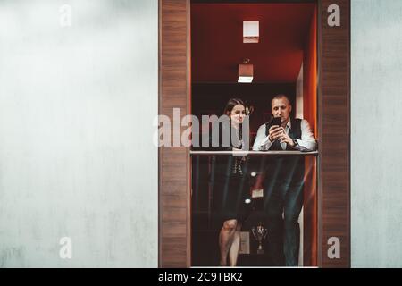 Due imprenditori che hanno un colloquio di affari mentre si levano in piedi sul balcone dell'ufficio: L'uomo d'affari sta mostrando un messaggio divertente sullo schermo di un telefono cellulare Foto Stock