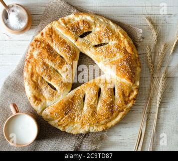 Torta rotonda su sackcloth, latte, sale e orecchie di grano e una tazza di latte, uno sfondo di legno chiaro Foto Stock