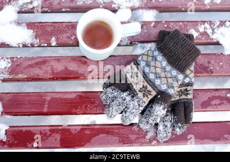 Tazza di tè e guanti in maglia da donna su una panca in inverno, la neve sotto. Vista dall'alto Foto Stock