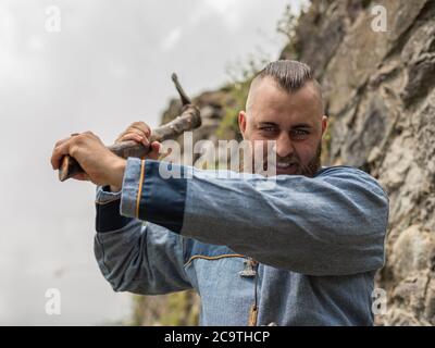 Un uomo in abiti medievali indossa un'ascia nelle rovine di un antico castello, una rievocazione storica vichinga Foto Stock