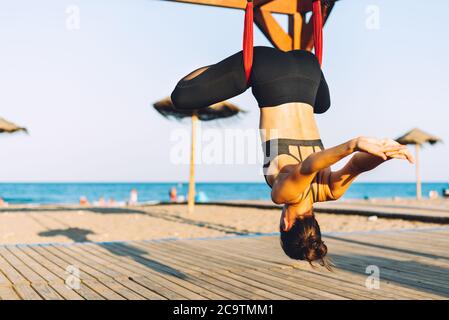 giovane donna che fa esercizi di yoga con swing capovolto sulla spiaggia di fronte al mare in una giornata di sole Foto Stock