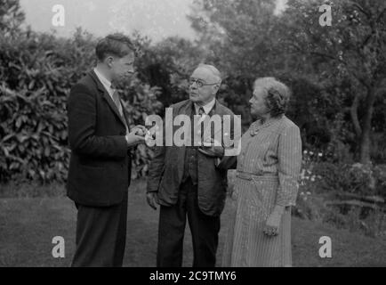 Anni '40, storico, un giovane in una giacca e cravatta in piedi fuori in un giardino posteriore che parla con i suoi genitori anziani, Inghilterra, Regno Unito. Foto Stock