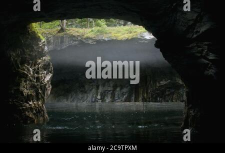 Vista dall'interno di una grotta allagata su un pendio di marmo durante la nebbia Foto Stock