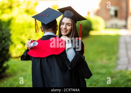 Abbracciando il suo amico, studente in mortarboard sentire abbracciare il suo amico, laureato in mortarboard. Sorridente laureato indossando mortarboard sensazione imprevedibile Foto Stock