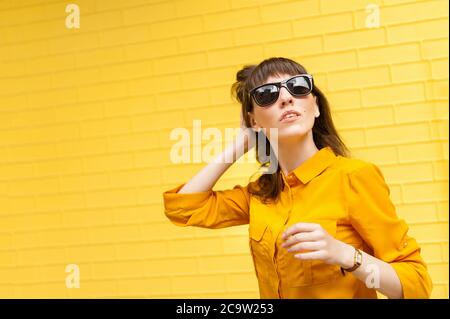 Giovane ragazza su sfondo giallo brillante in camicia gialla raddrizza i capelli. Foto Stock