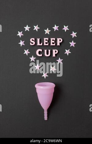 Coppa mestruale rosa su sfondo nero con cuore e parole Coppa Sleep. Concetto possibilità di utilizzare la tazza di notte, zero sprechi, risparmio, minimalismo. Foto Stock