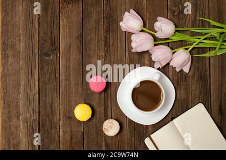 Tazza di caffè, macaron, tulipani rosa e taccuino su sfondo di legno. Vista dall'alto Foto Stock