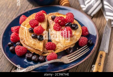 Frittelle dolci fatte in casa con lamponi e mirtilli su piatto blu su scrivania di legno scuro. Foto Stock