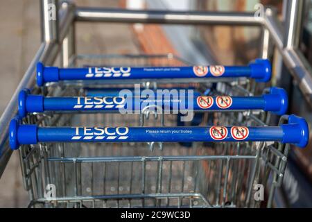 Un primo piano delle maniglie dei carrelli per lo shopping Tesco o dei carrelli per lo shopping in un parcheggio di tram Foto Stock