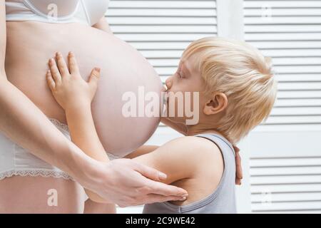 Cute baby boy baciare e abbracciare la pancia della mamma incinta. Secondo concetto di gravidanza Foto Stock