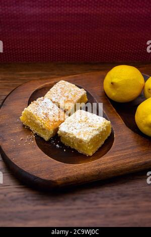 Quadrati di limone cotti in casa, barrette di limone, con limoni su uno sfondo di legno sfocato in orientamento ritratto Foto Stock