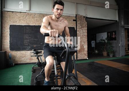 Uomo che usa la bicicletta da ginnastica in palestra. Fitness maschile utilizzando la moto d'aria per l'allenamento cardio alla palestra di allenamento funzionale Foto Stock