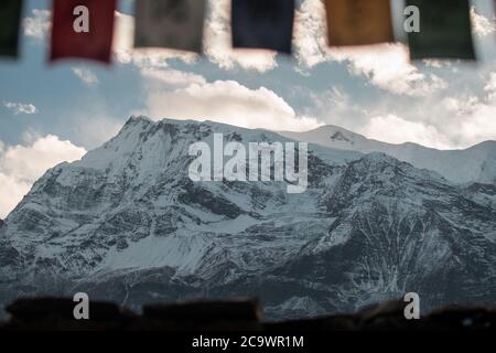 Bandiere buddiste di preghiera nelle montagne nepalesi innevate, circuito di Annapurna, Himalaya Foto Stock