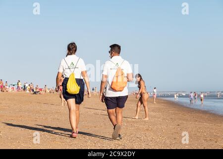 Punta Umbria, Huelva, Spagna - 2 agosto 2020: Guardia di sicurezza della spiaggia di Junta de Andalucia sta controllando l'allontanamento sociale e l'uso della maschera protettiva Foto Stock