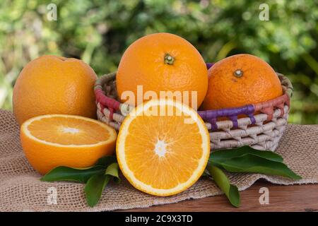 Mature arance intere e pezzi tagliati in cestino su tavola di legno con sfondo verde sfocato. Spazio di copia Foto Stock