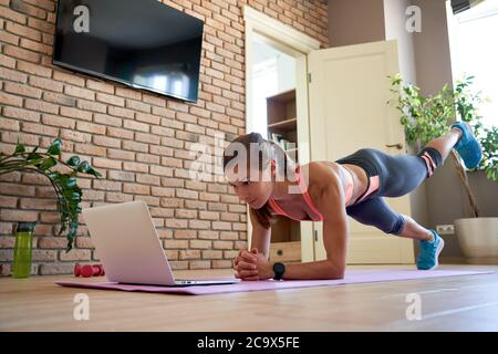 Adatta giovane donna sportiva facendo esercizio di allenamento online guardando video a casa. Foto Stock