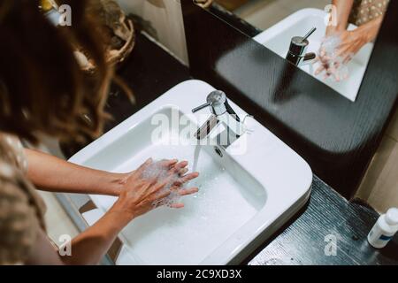 Vista dall'alto delle mani della donna mentre lavate le mani con sapone in bagno. Prevenzione di COVID - 19 coronavirus Foto Stock