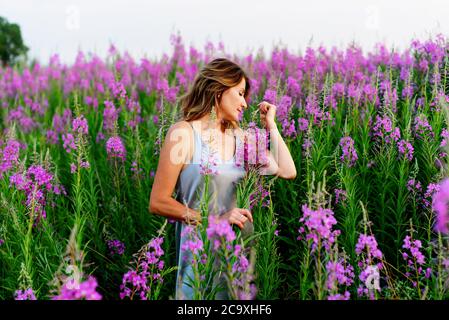 Bella donna in abito grigio si rilassa con mazzo di fiori sul prato di fireweed Foto Stock