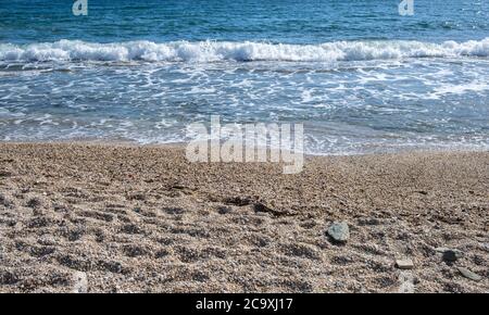 Spiaggia di sabbia, onde morbide che si ondeggia sulla riva, riflessi sull'acqua di mare, sfondo di spiaggia vuoto nelle prime ore del mattino. Foto Stock