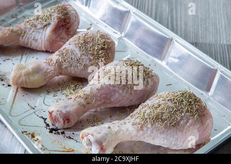 Cosce di bastone di pollo crudo ricoperte di rosmarino in una teglia da forno a lamina Foto Stock