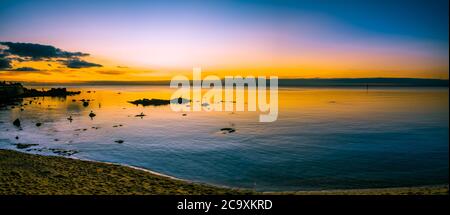 Mare panoramico di un tramonto luminoso sulle calme acque della baia dell'oceano con rocce e silhouette di uccelli Foto Stock