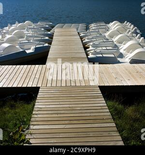 File di pedalò in affitto lungo un pontile di legno, Lago Chambon , Puy de Dome, Auvergne, Francia Foto Stock