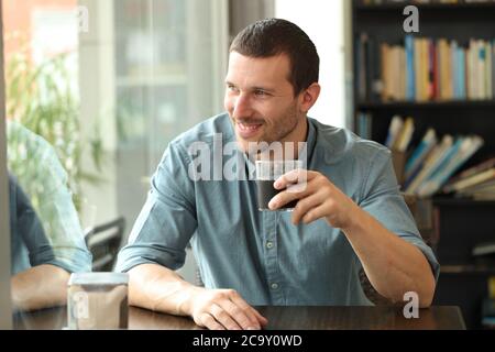 Uomo felice che guarda via la finestra di lancio seduto in un tavolino di una caffetteria che tiene il vetro Foto Stock