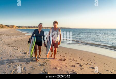 Coppia matura con tavole da surf sulla bellissima spiaggia godendo di paradiso e di uno stile di vita attivo. Bella forma uomo e donna surf e divertirsi. In trave Foto Stock