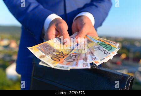 Concetto di tangenti e affari. La mano maschio tiene le fatture del dollaro. L'uomo mostra le banconote in primo piano. Businessmans mani con soldi vicino al caso nero sopra Foto Stock