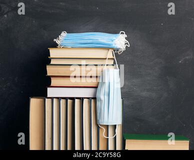 stack di vari libri e maschere mediche monouso sullo sfondo di una lavagna vuota in gesso nero, concetto di visitare le biblioteche in protec personale Foto Stock