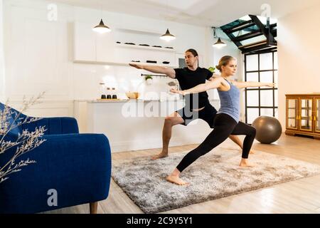 Una coppia sportiva bianca caucasica che fa da guerriero yoga posa in salotto a casa. Allenarsi, sport fitness e stile di vita sano. Foto Stock