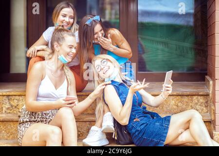 Giovani donne alla moda con maschere aperte divertirsi in videochiamata con gli amici durante le vacanze estive Foto Stock