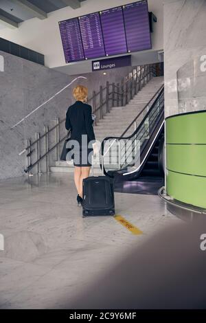 Donna elegante con valigia da viaggio in piedi al terminal dell'aeroporto Foto Stock