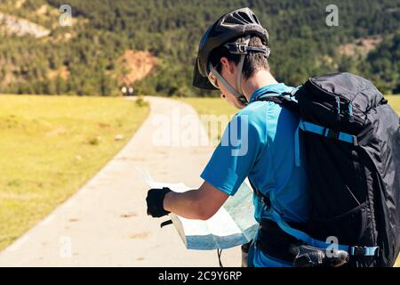 giovane biker con zaino e mountain bike in piedi su un percorso mentre si consulta il suo percorso sulla mappa, concetto di sport e sano stile di vita in natura Foto Stock