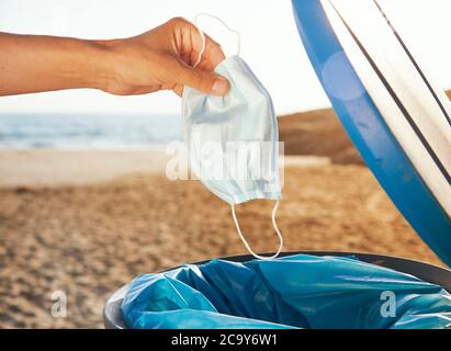 primo piano di un uomo caucasico che lancia una maschera usata al cestino della spazzatura sulla spiaggia Foto Stock