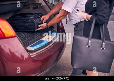 Un driver maschile aiuta la signora a mettere i bagagli nel bagagliaio dell'auto Foto Stock