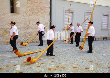 I giocatori svizzeri di alphorn si preparano a dare un concerto il giorno nazionale svizzero, fuori dalla chiesa abbaziale di Notre-Dame a Payerne, cantone o Foto Stock