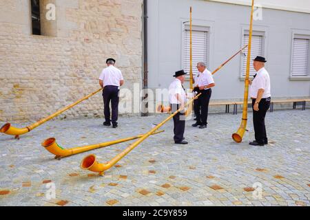 I giocatori svizzeri di alphorn si preparano a dare un concerto il giorno nazionale svizzero, fuori dalla chiesa abbaziale di Notre-Dame a Payerne, cantone o Foto Stock