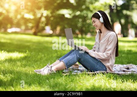 Happy Asian Girl Freelancer lavorando su laptop in Park e ascoltare musica Foto Stock