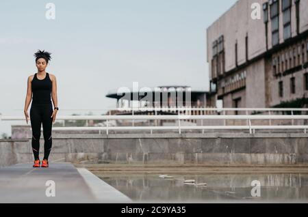 Bella atletica sportiva in strada. Ragazza afroamericana con occhi chiusi, in abbigliamento sportivo, con tracker fitness Foto Stock