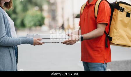 Prelievo e consegna. Uomo di consegna con zaino, orologi intelligenti dare scatole con pizza per la ragazza in casual Foto Stock