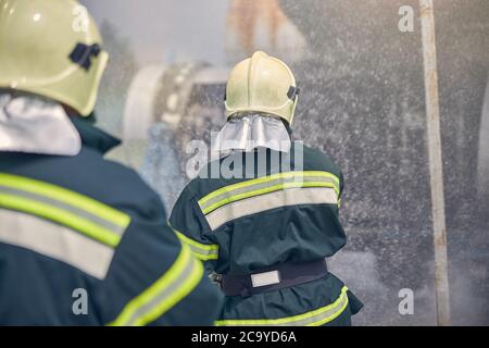 Due vigili del fuoco con uniforme ignifuga in piedi accanto a un luogo di emergenza Foto Stock