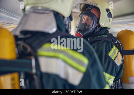 Due vigili del fuoco con attrezzature complete in piedi nel luogo di emergenza Foto Stock