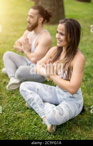 Vacanze estive, Vacanze attività, amore e sport concetto di stile di vita - felice coppia giovane in activewear seduti sul prato verde nella posizione del loto, m Foto Stock
